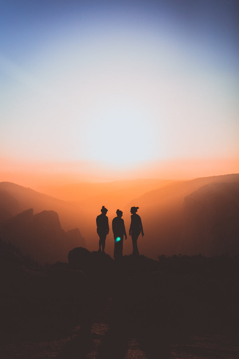 Silhouettes de trois personnes sur un sommet de montagne au coucher du soleil, évoquant l’amitié, l’aventure et le dépassement de soi.