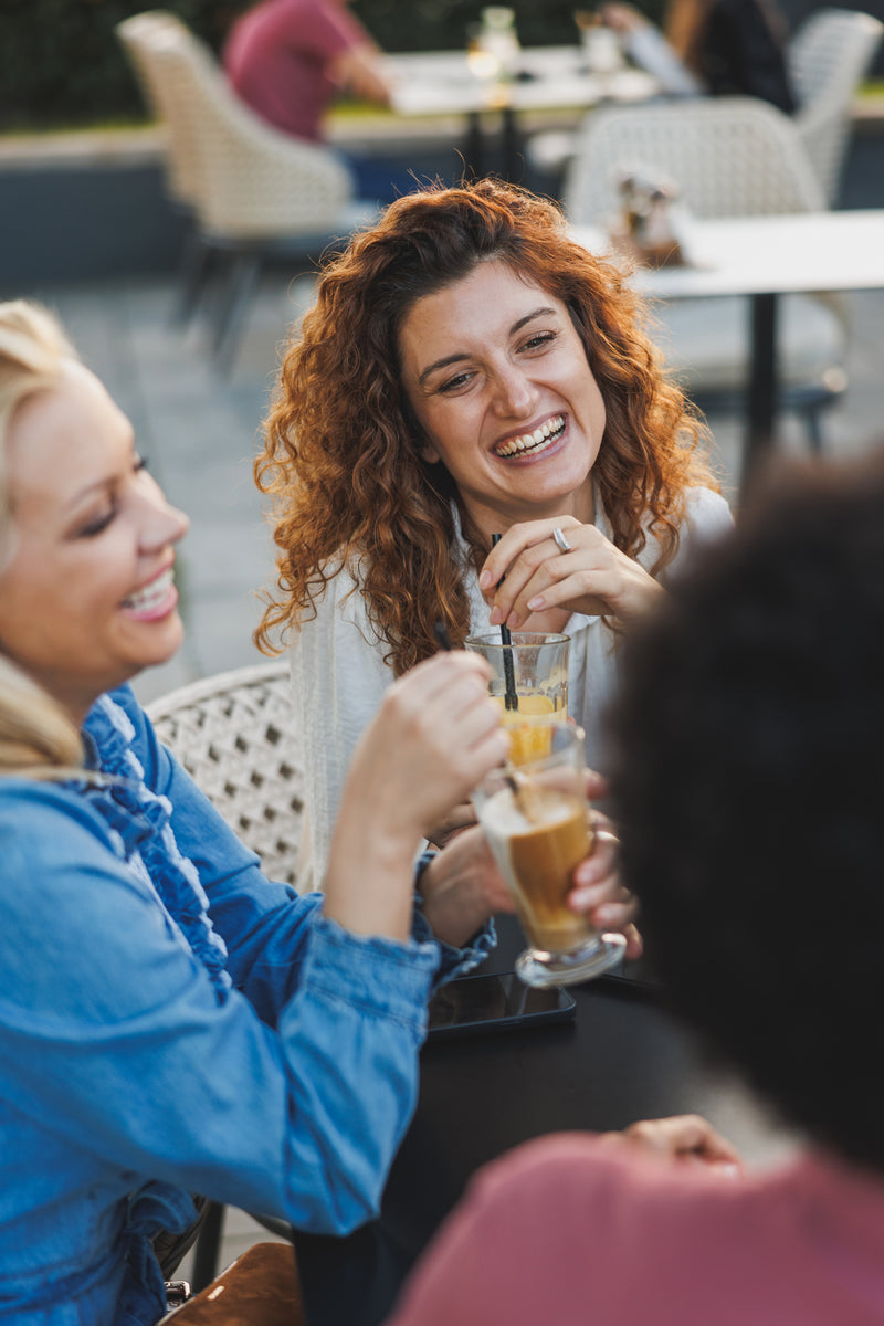 Amies réunies autour de boissons et discutant à une table en terrasse.