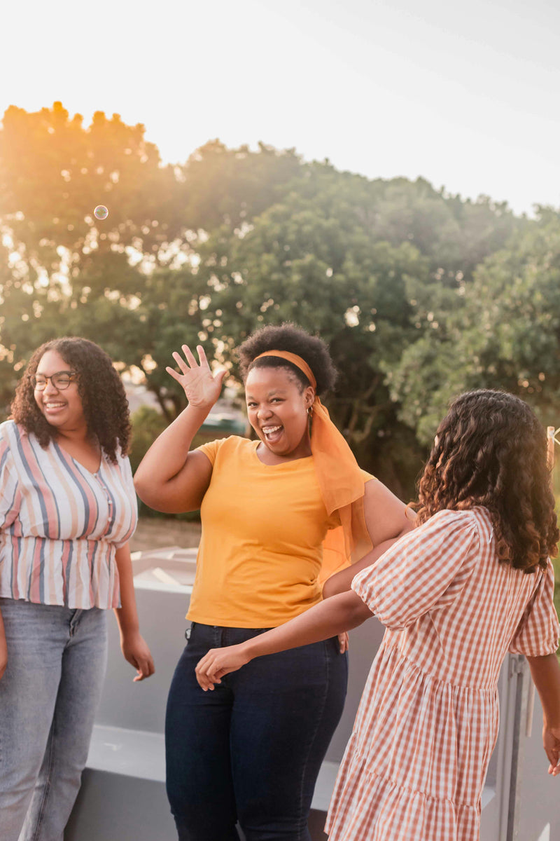 Femmes dansant et souriant en plein air à la lumière du soleil couchant.