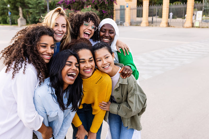 Groupe de femmes souriantes se tenant dans les bras en extérieur.
