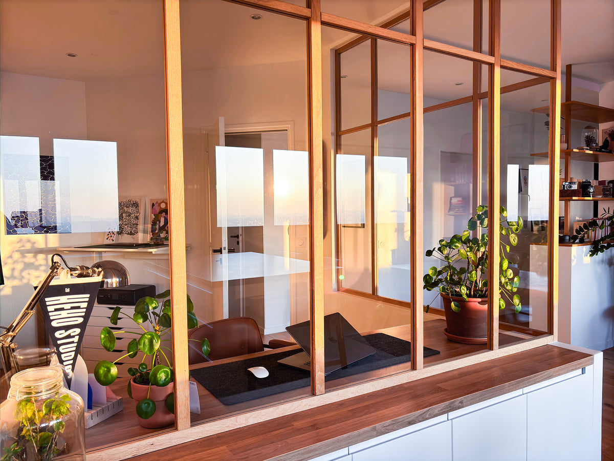 Bureau derrière verrière en bois dans un intérieur contemporain lumineux avec plantes, mobilier design et lumière de fin de journée.