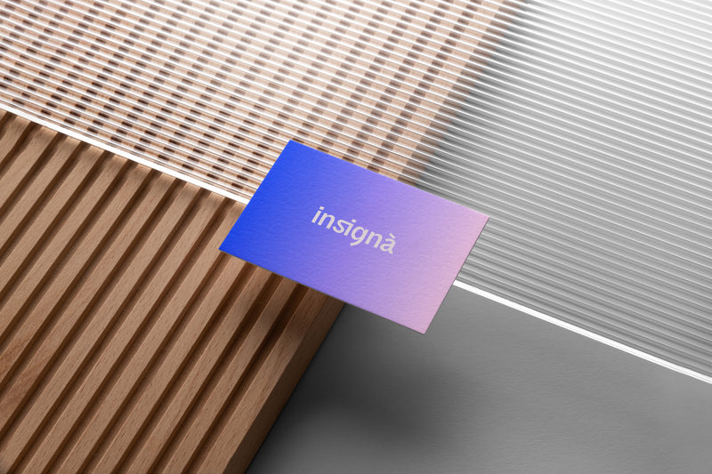 Carte de visite Insignà en dégradé bleu-violet-rose, vue macro sur fond de lattes de bois.