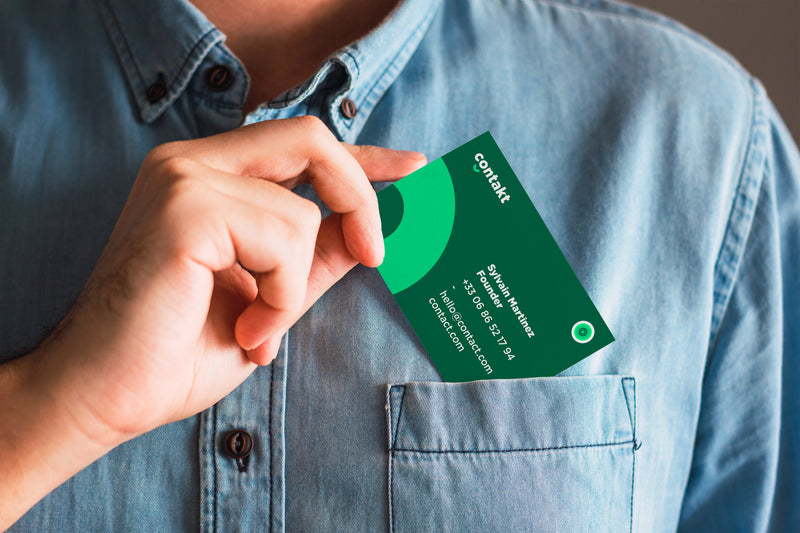 Carte de visite verte au design minimaliste représentant une identité visuelle éco-responsable, glissée dans la poche d’une chemise.