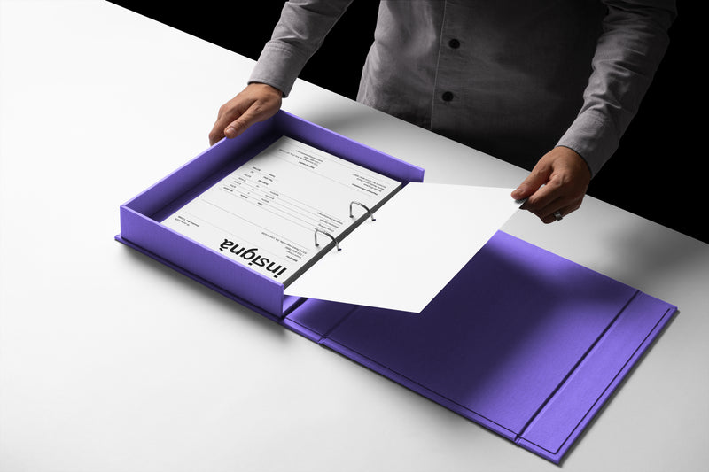 Classeur à anneaux violet ouvert présentant une facture Insignà, tenu par une main qui en tourne une page.