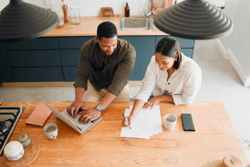 Couple analysant des documents financiers et utilisant un ordinateur portable pour préparer un projet de crédit ou d’investissement immobilier.