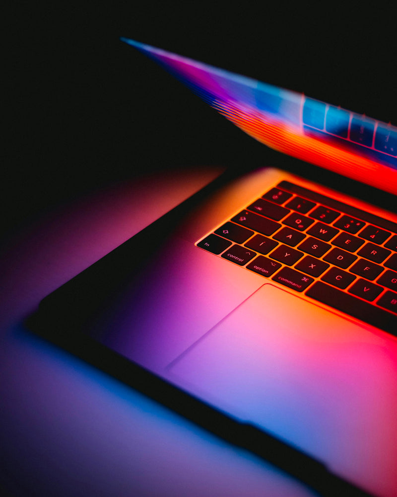 Clavier d’ordinateur portable éclairé par des lumières néon rouges et bleues dans une ambiance digitale créative et contemporaine.