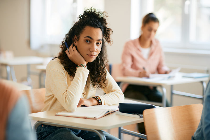 Étudiante assise en classe prenant des notes pendant un cours dans une salle de classe lumineuse.
