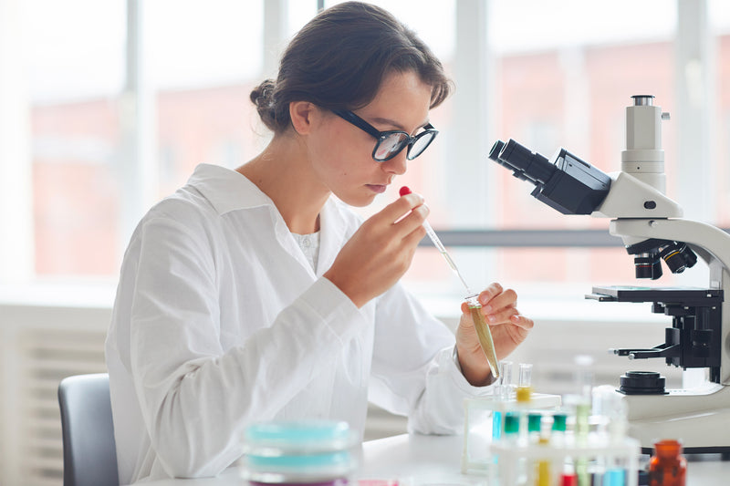 Étudiante en laboratoire réalisant une analyse scientifique avec pipette et microscope dans un environnement de recherche médicale.