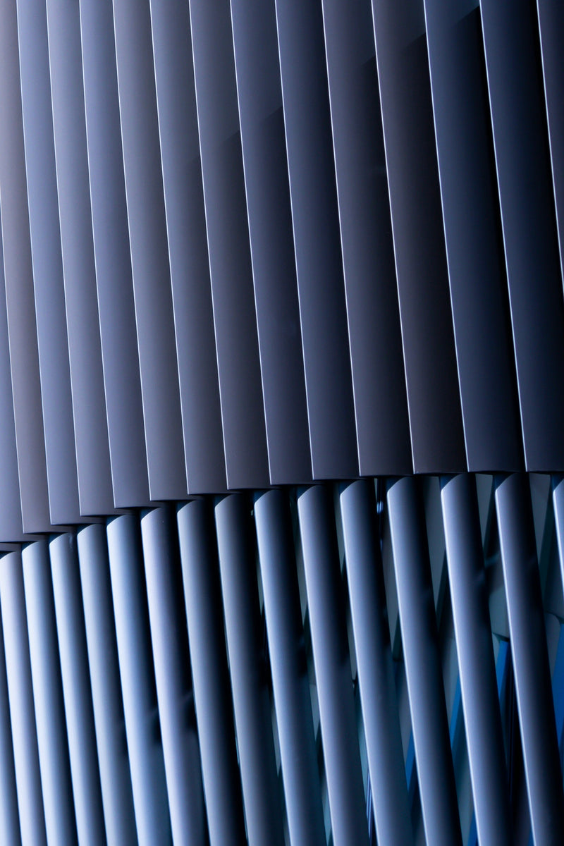 Gros plan sur une façade architecturale en lames métalliques verticales bleu-gris, effet plissé.