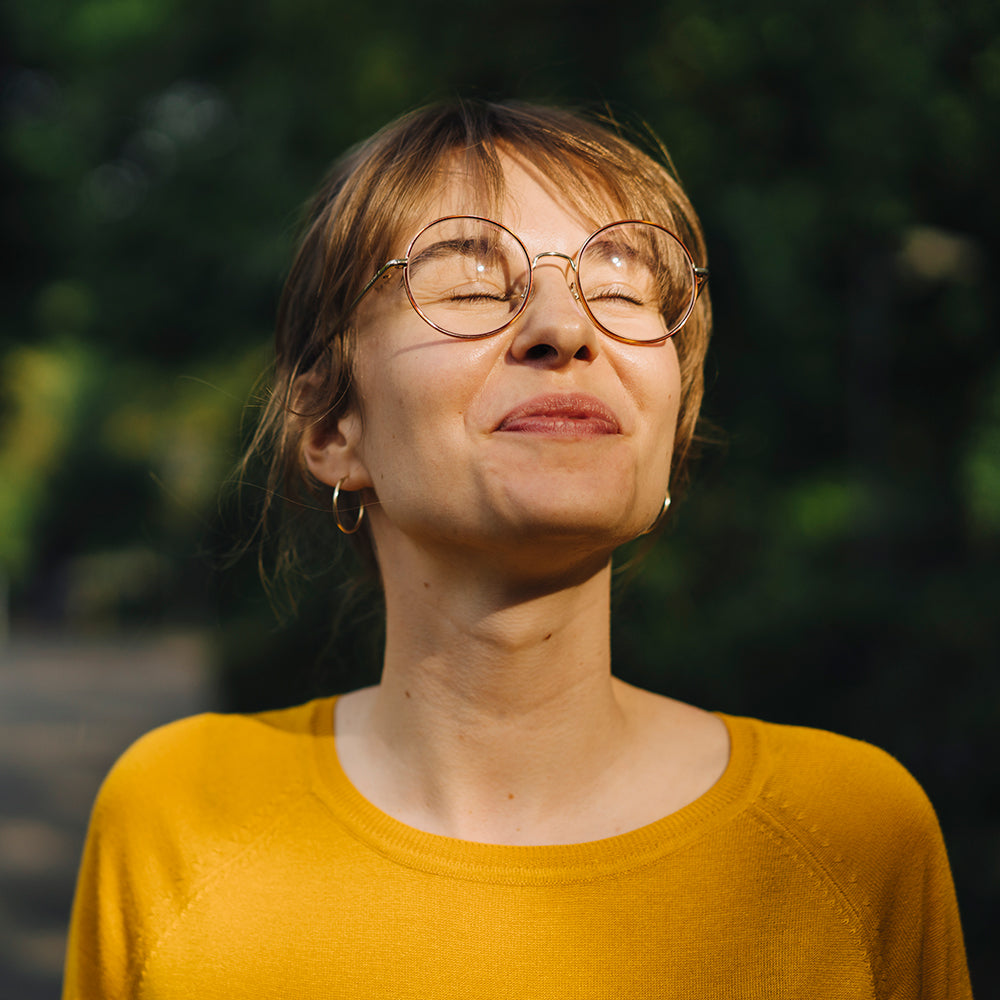 Portrait d’une femme souriante en extérieur, yeux fermés, évoquant un sentiment de liberté et de sérénité financière.