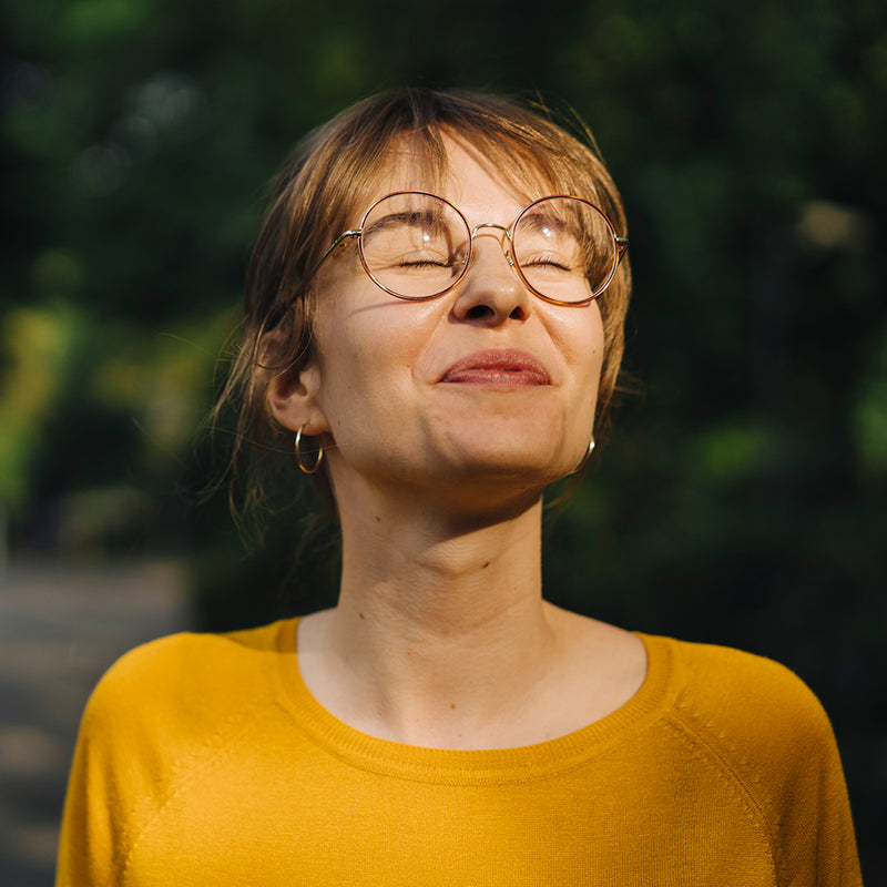 Portrait d’une femme souriante en extérieur, yeux fermés, évoquant un sentiment de liberté et de sérénité financière.