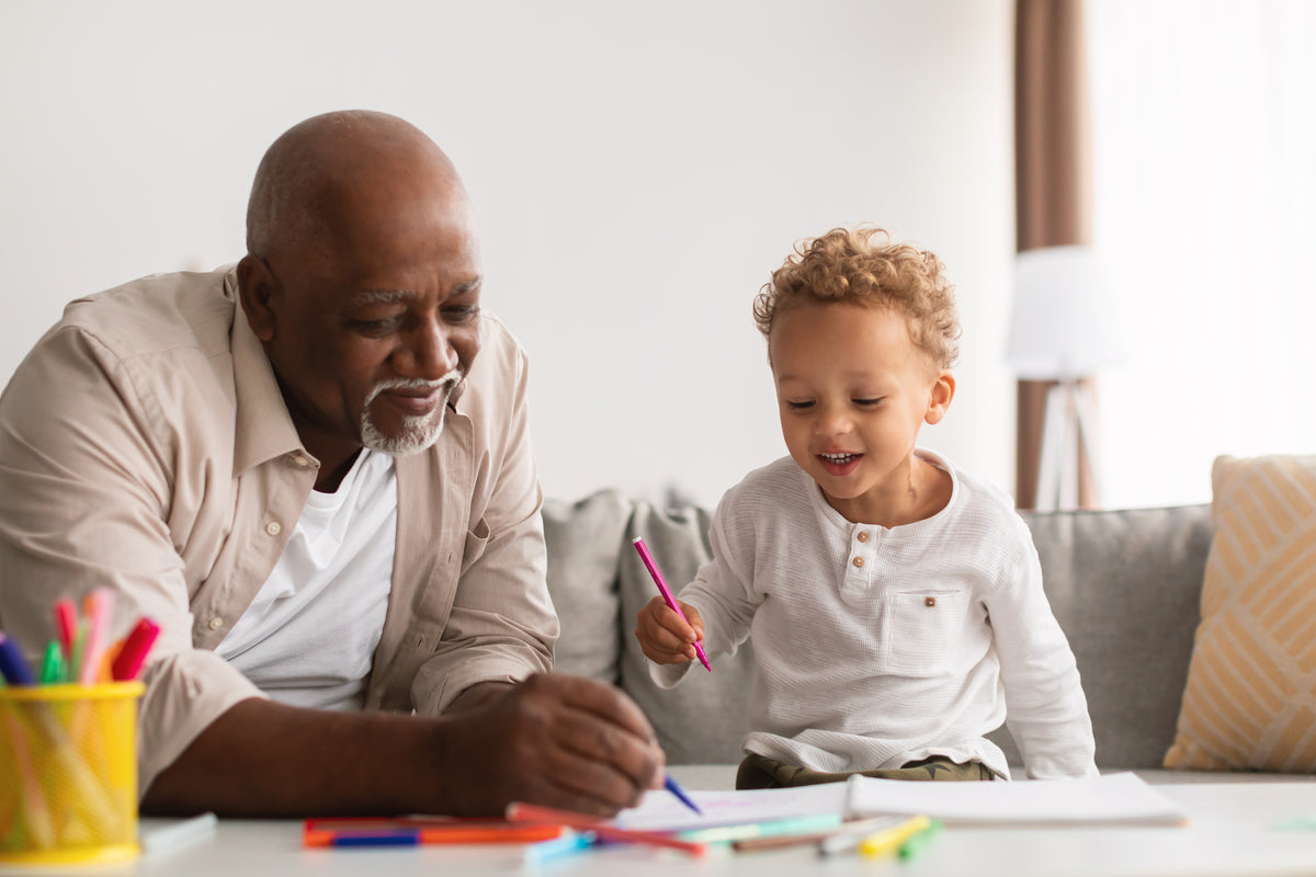 Grand-père et enfant dessinant ensemble à la maison, moment de complicité familiale autour d’une activité créative.