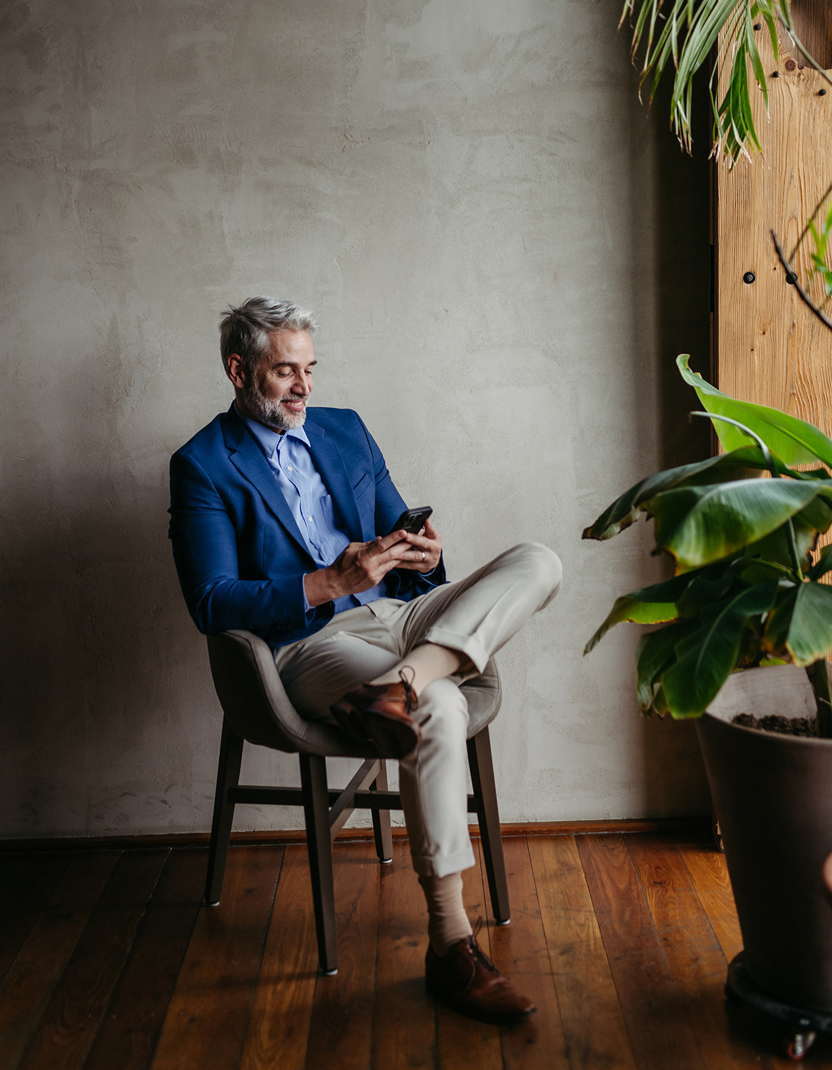 Homme assis sur une chaise consultant son smartphone dans un intérieur moderne, évoquant la gestion ou l’investissement immobilier en ligne.