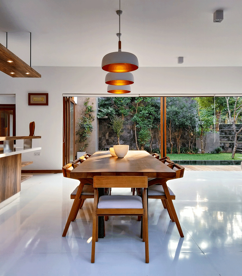 Intérieur de maison moderne avec salle à manger en bois et grandes baies vitrées donnant sur un jardin.