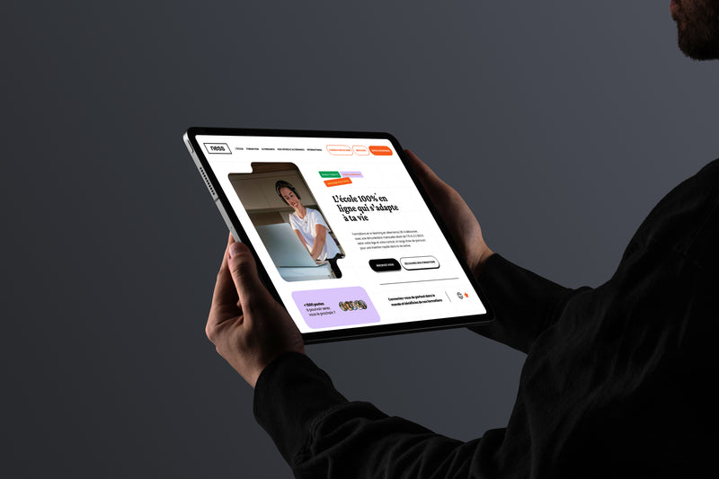 Page d’accueil du site Ness School affichée sur une tablette tenue à deux mains.