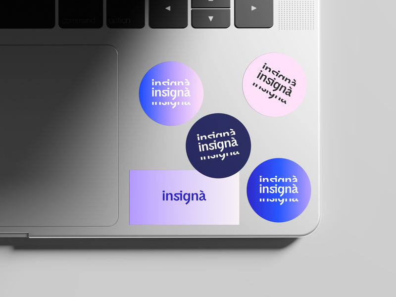 Stickers ronds et carrés du logo Insignà posés sur le coin d'un MacBook.