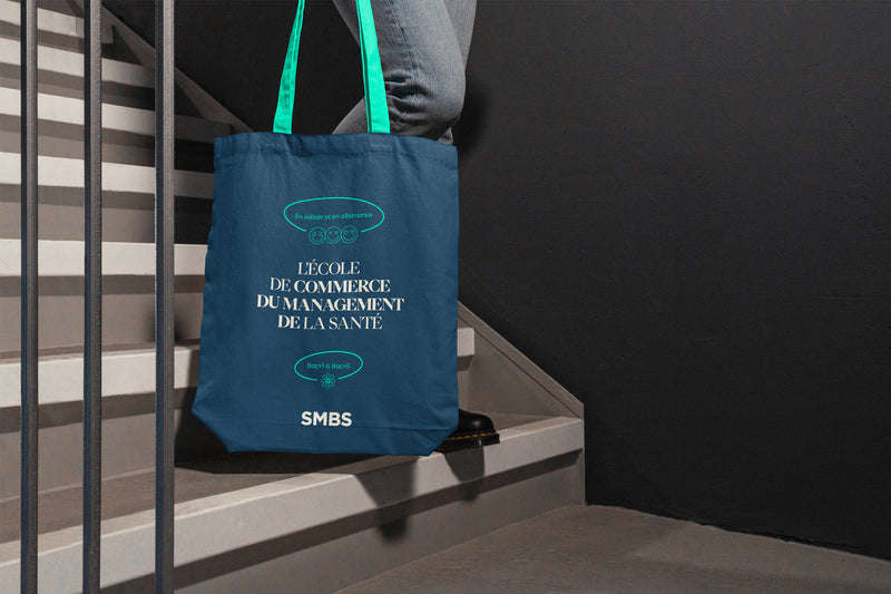 Tote bag promotionnel d’une école de commerce spécialisée en management de la santé porté dans un escalier.