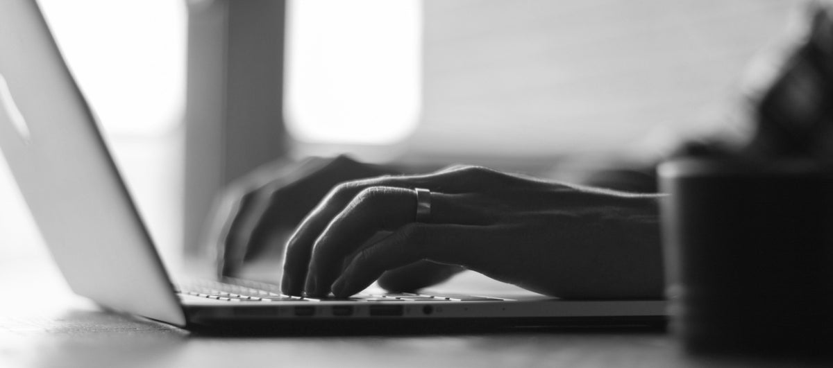 Mains en train de travailler sur un ordinateur portable dans un contexte de création graphique, ambiance studio design en noir et blanc.