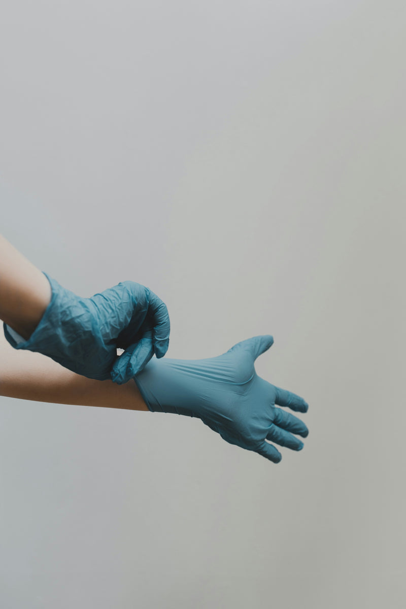 Soignant enfilant des gants médicaux bleus.